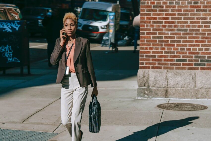 woman walking along sidewalk with briefcase with mobile phone