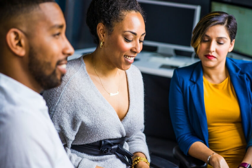 three people seated in office looking at laptop