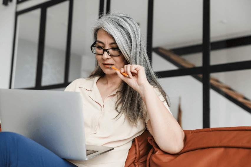 Woman on couch looks at open laptop on her lap.